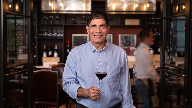 Master Sommelier George Miliotes holding a glass of wine, standing in Wine Bar George restaurant