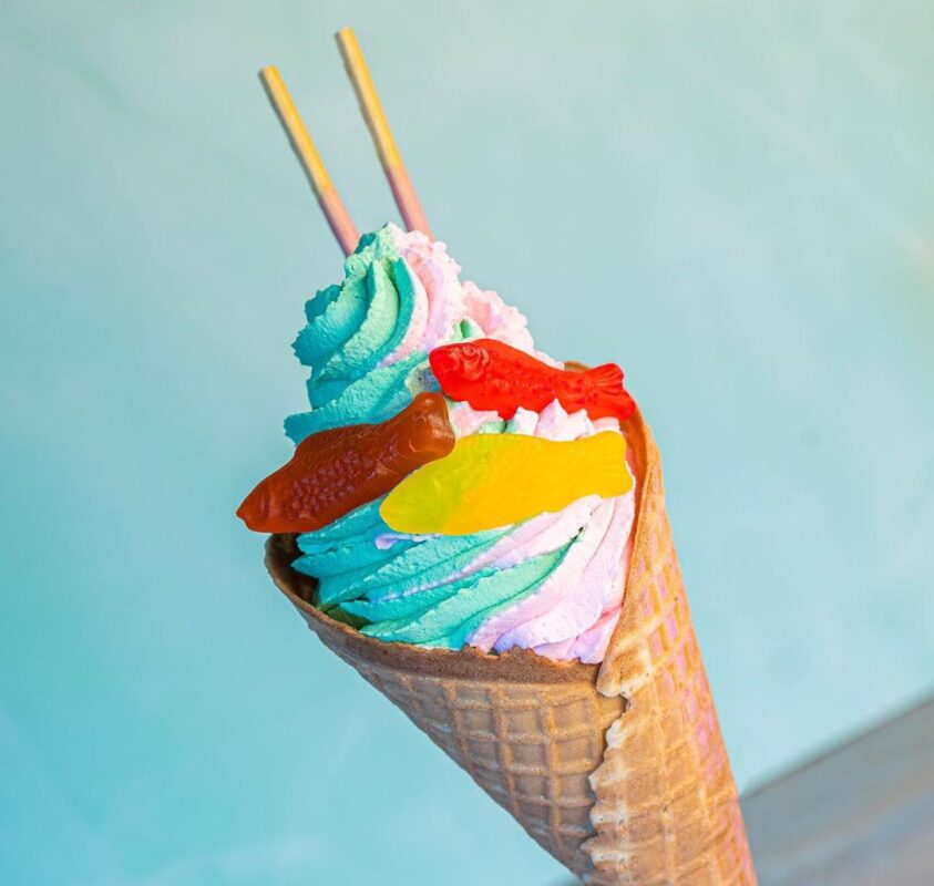 Waffle cone filled with blue and pink swirled ice cream, topped with colorful gummy fish and two thin wafer sticks—a delightful addition to the new menu items at Disney H2O Glow, Typhoon Lagoon Water Park.