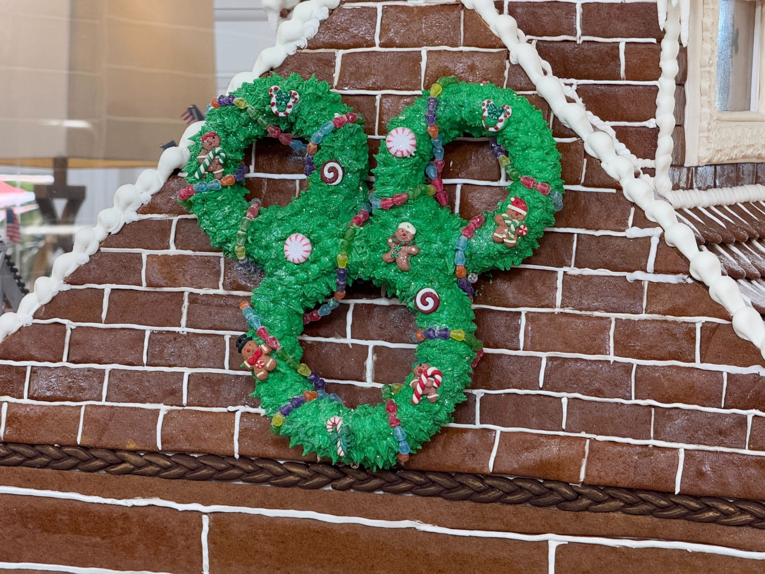 A gingerbread house roof decorated with a green wreath shaped like a character's head, featuring candy canes and a gingerbread figure.