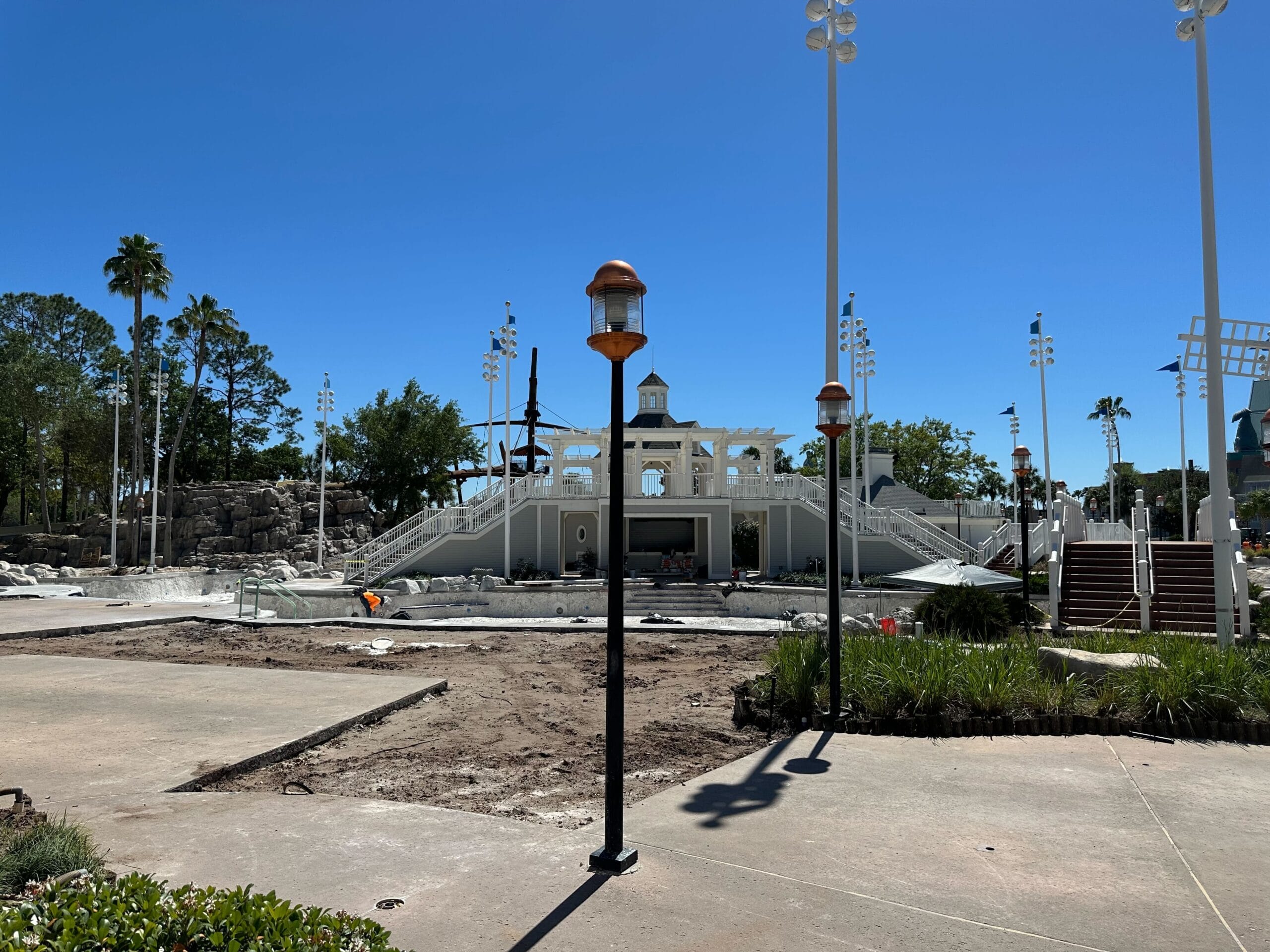 View of a construction site near Disney’s Yacht Club, featuring a partially built structure surrounded by lights and trees. A clear blue sky is in the background, and the ground appears mostly dirt with patches of grass—much like the serene surroundings of Stormalong Bay Pool. View of a construction site near Disney’s Yacht Club, featuring a partially built structure surrounded by lights and trees. A clear blue sky is in the background, and the ground appears mostly dirt with patches of grass—much like the serene surroundings of Stormalong Bay Pool.