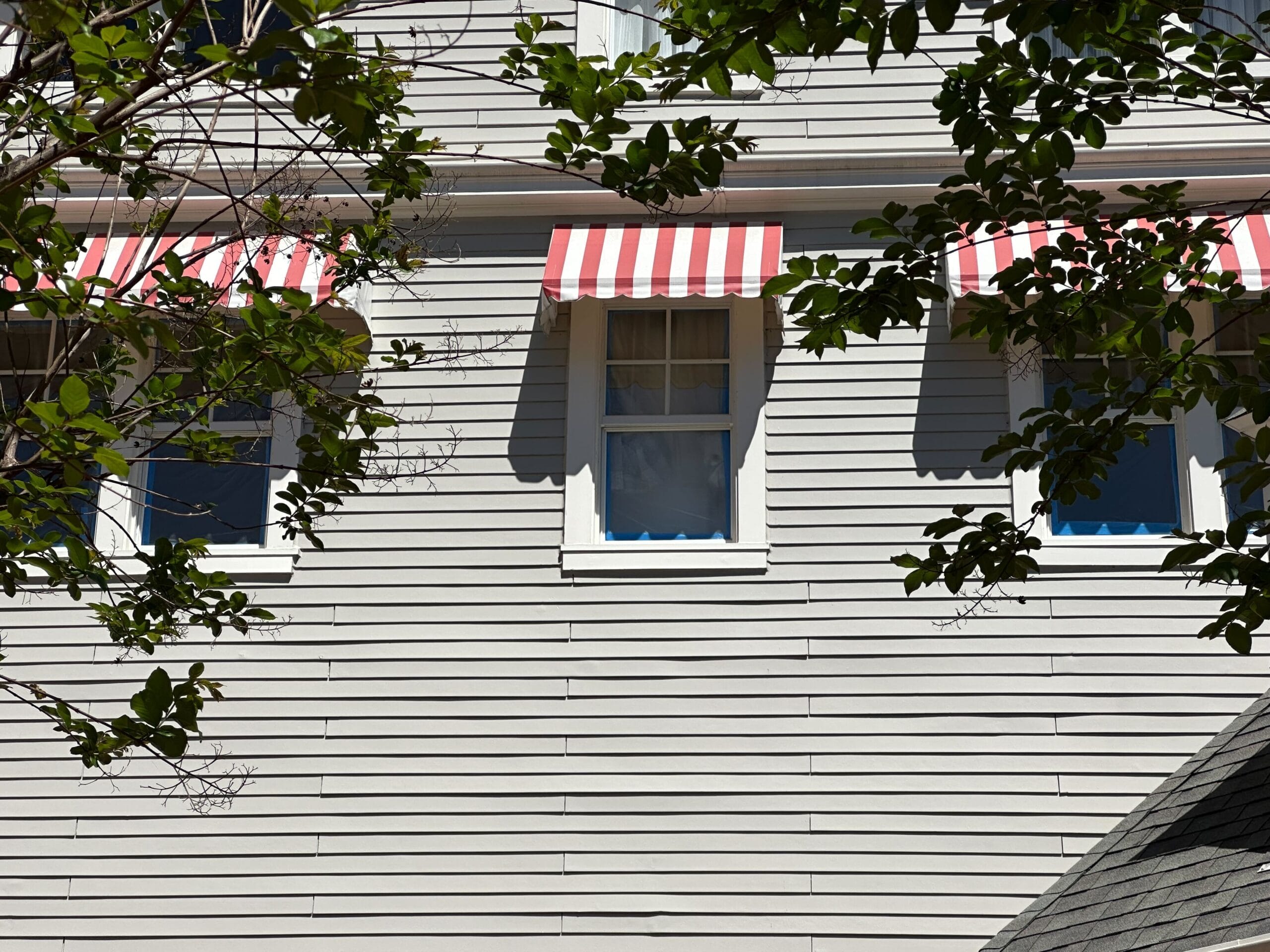 A beige building with three windows, each adorned with a red and white striped awning reminiscent of Disney’s Yacht Club charm. Tree branches gracefully overlap the view, adding a touch of nature to this picturesque scene. A beige building with three windows, each adorned with a red and white striped awning reminiscent of Disney’s Yacht Club charm. Tree branches gracefully overlap the view, adding a touch of nature to this picturesque scene.