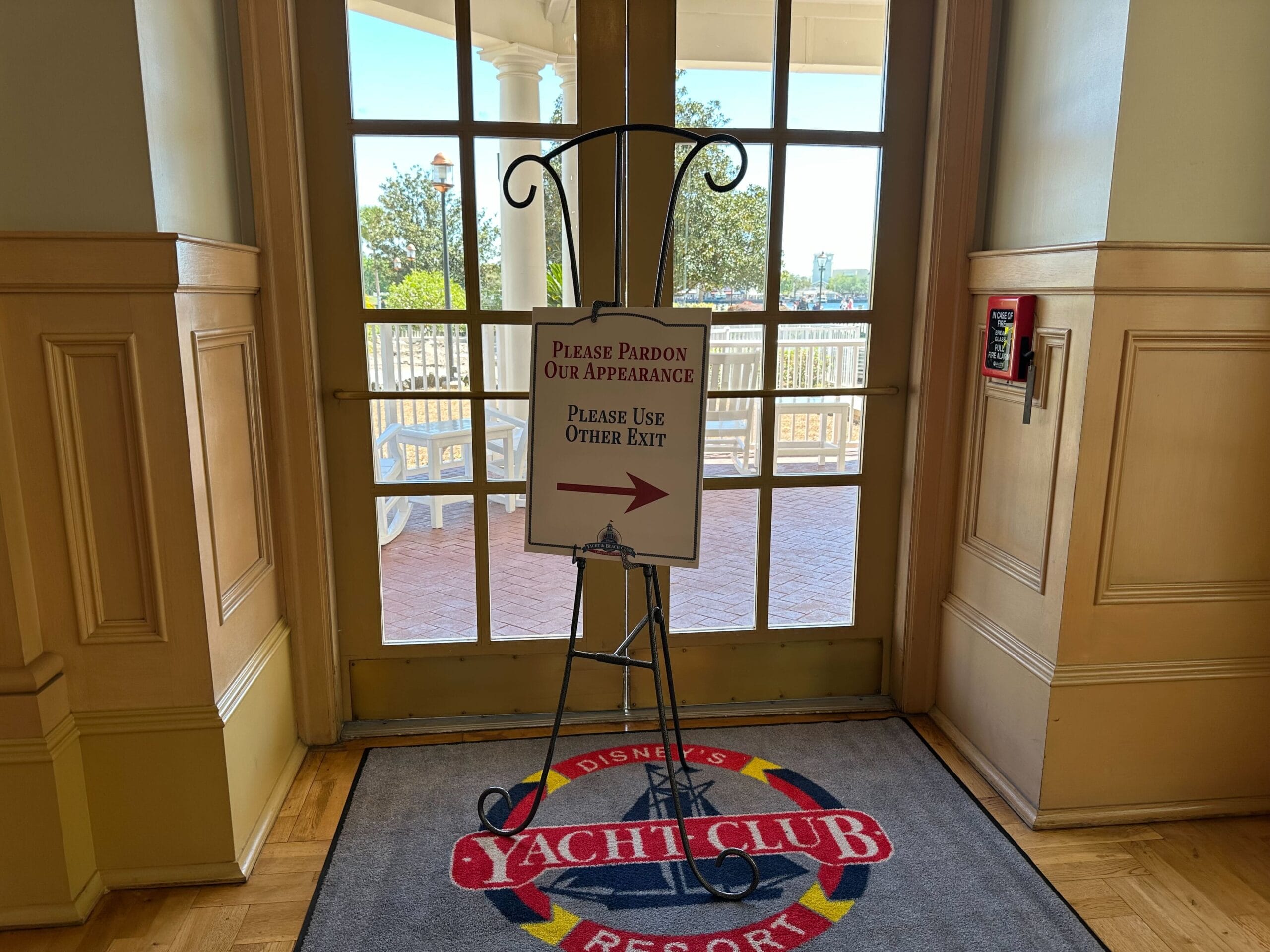 A sign on an easel at Disney's Yacht Club Resort directs guests to use an alternative exit due to ongoing construction. The backdrop features tile and a glimpse of the outdoor scenery, hinting at the nearby Stormalong Bay Pool. A sign on an easel at Disney's Yacht Club Resort directs guests to use an alternative exit due to ongoing construction. The backdrop features tile and a glimpse of the outdoor scenery, hinting at the nearby Stormalong Bay Pool.