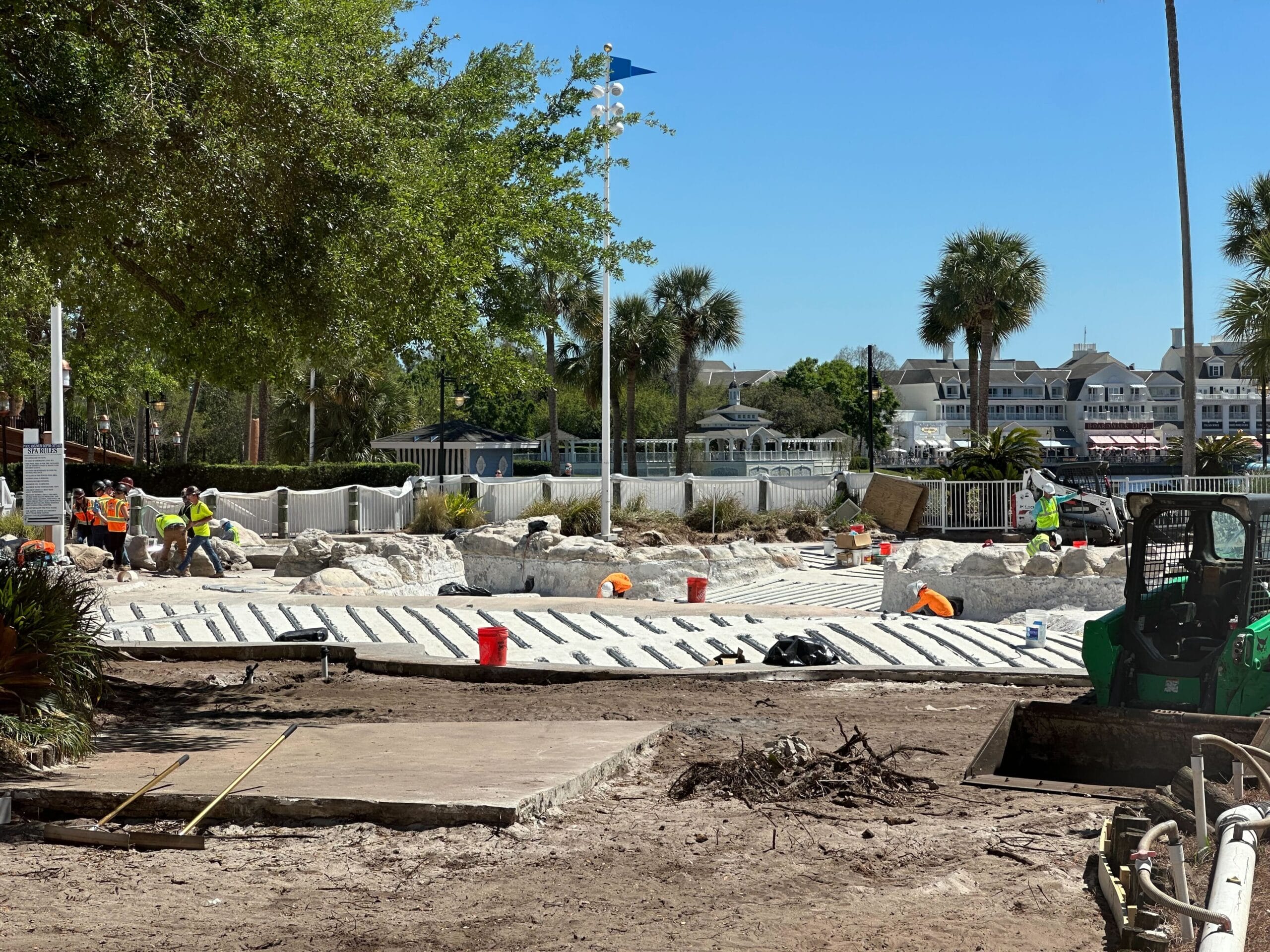 At the construction site, workers are carefully installing striped paving stones. Equipment and materials lie scattered, while trees and buildings rise in the background under a clear blue sky, reminiscent of the serenity found around Disney's Yacht Club. At the construction site, workers are carefully installing striped paving stones. Equipment and materials lie scattered, while trees and buildings rise in the background under a clear blue sky, reminiscent of the serenity found around Disney's Yacht Club.